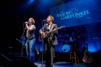 Two young men passionately sing into microphones on stage at "The Graduates – The Sound of Simon & Garfunkel" in Big Bear.