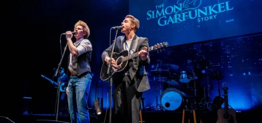 Two young men passionately sing into microphones on stage at "The Graduates – The Sound of Simon & Garfunkel" in Big Bear.