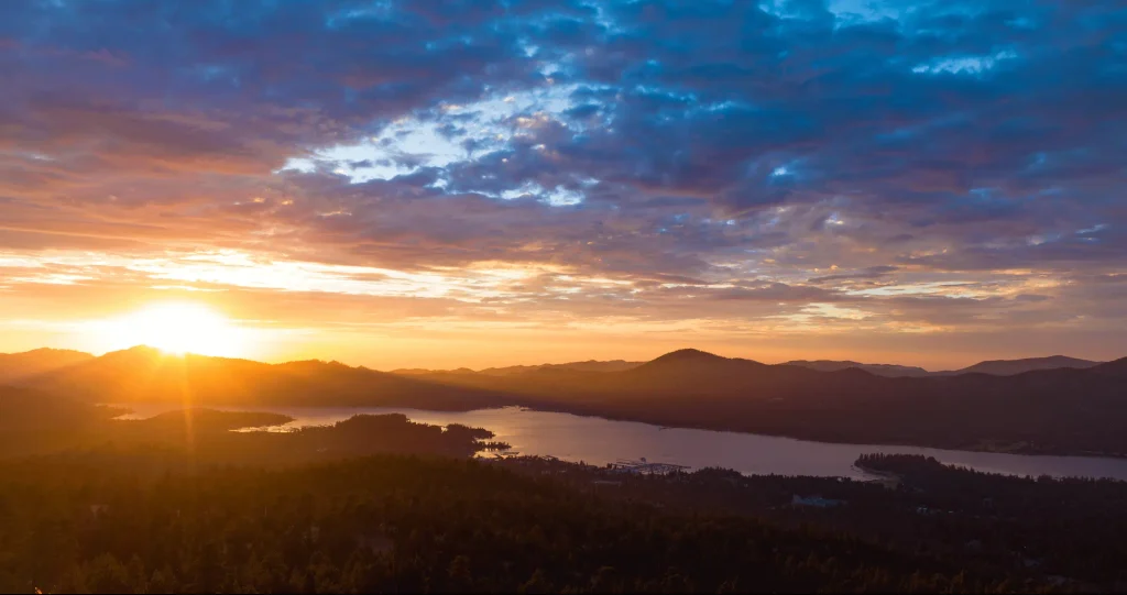 A serene sunset over a lake, with mountains silhouetted against the vibrant sky at Big Bear.