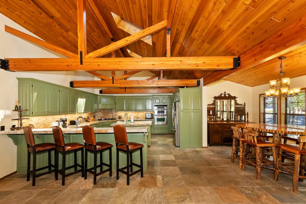A rustic kitchen and dining area with green cabinets, wooden beams, and a large dining table in Big Bear.