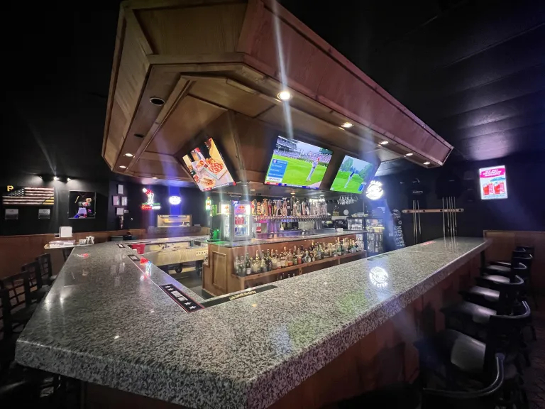 Sports bar interior featuring a granite bar counter, multiple televisions, and a selection of drinks on display
