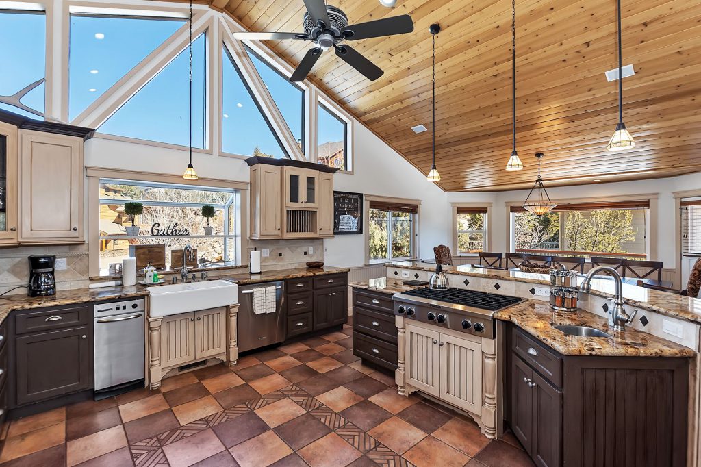 A spacious kitchen with brown and beige cabinets, granite countertops, and a large island with a gas cooktop in the center, and a large window with a view of the mountains in Big Bear.