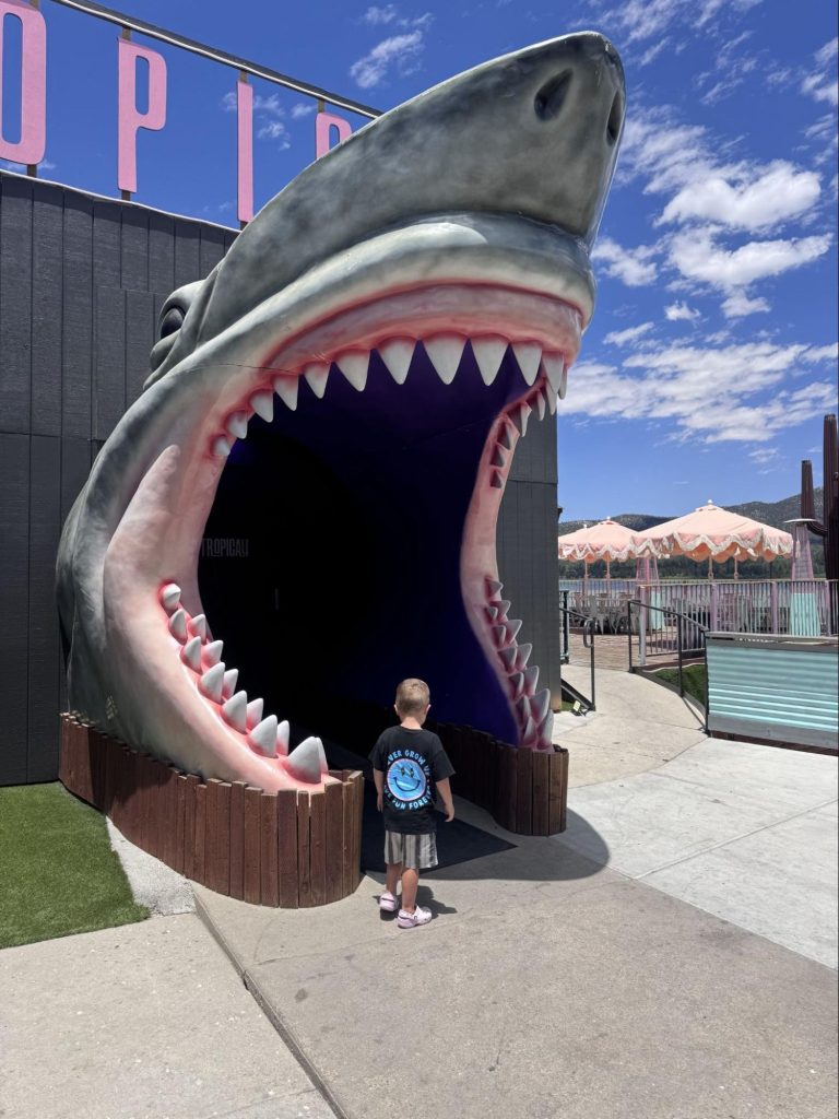 Child standing at the giant shark entrance to TropiKali on the Big Bear Lake waterfront.