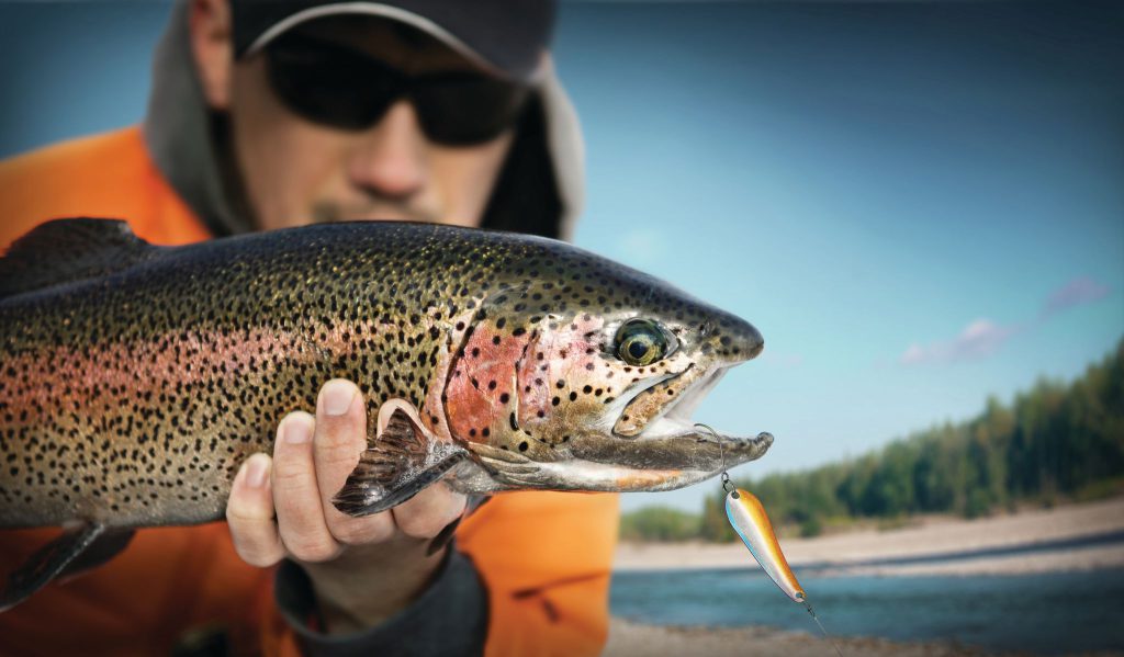 A man holds a large rainbow trout with a lure in its mouth, showing off his catch from Big Bear Lake.
