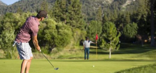 A man prepares to putt on a golf course at Big Bear with forested mountains in the background.