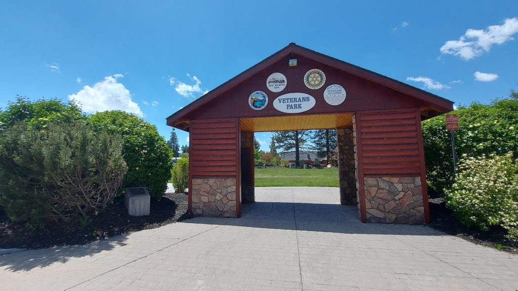 Entrance structure to Veterans Park in Big Bear Lake featuring a rustic wooden archway with park signage, landscaped greenery, and a clear blue sky.