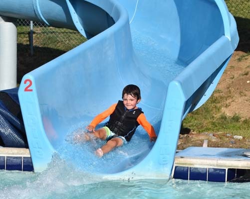 A young boy splashes down a blue water slide into a pool at a waterpark in Big Bear.