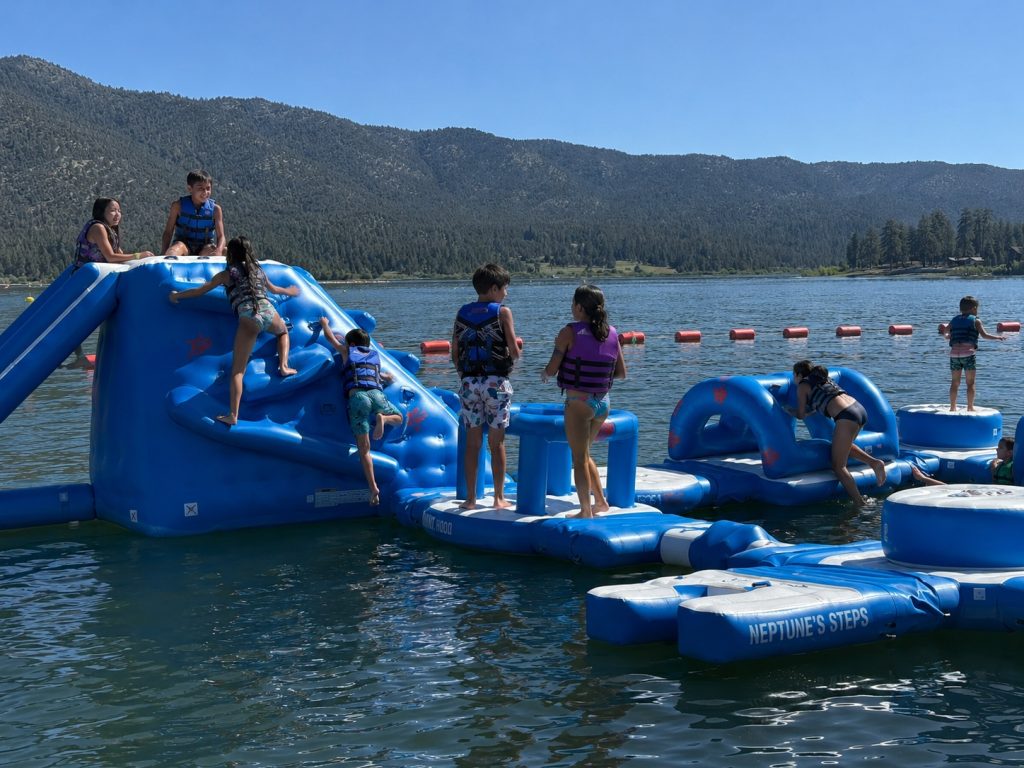Children playing on a floating inflatable water park obstacle course on a mountain lake during summer