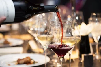 A stream of red wine is being poured into a clear wine glass against a dark background at Big Bear
