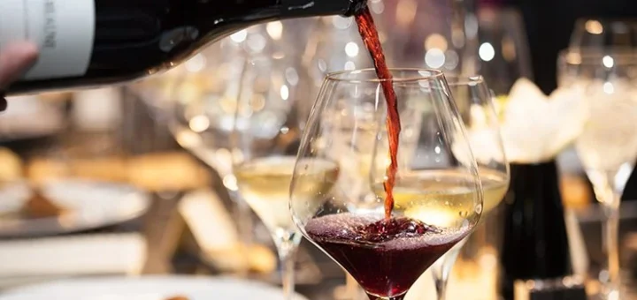 A stream of red wine is being poured into a clear wine glass against a dark background at Big Bear